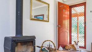 Um quarto com uma lareira a lenha, uma cesta de vime, um cão e uma porta vermelha.