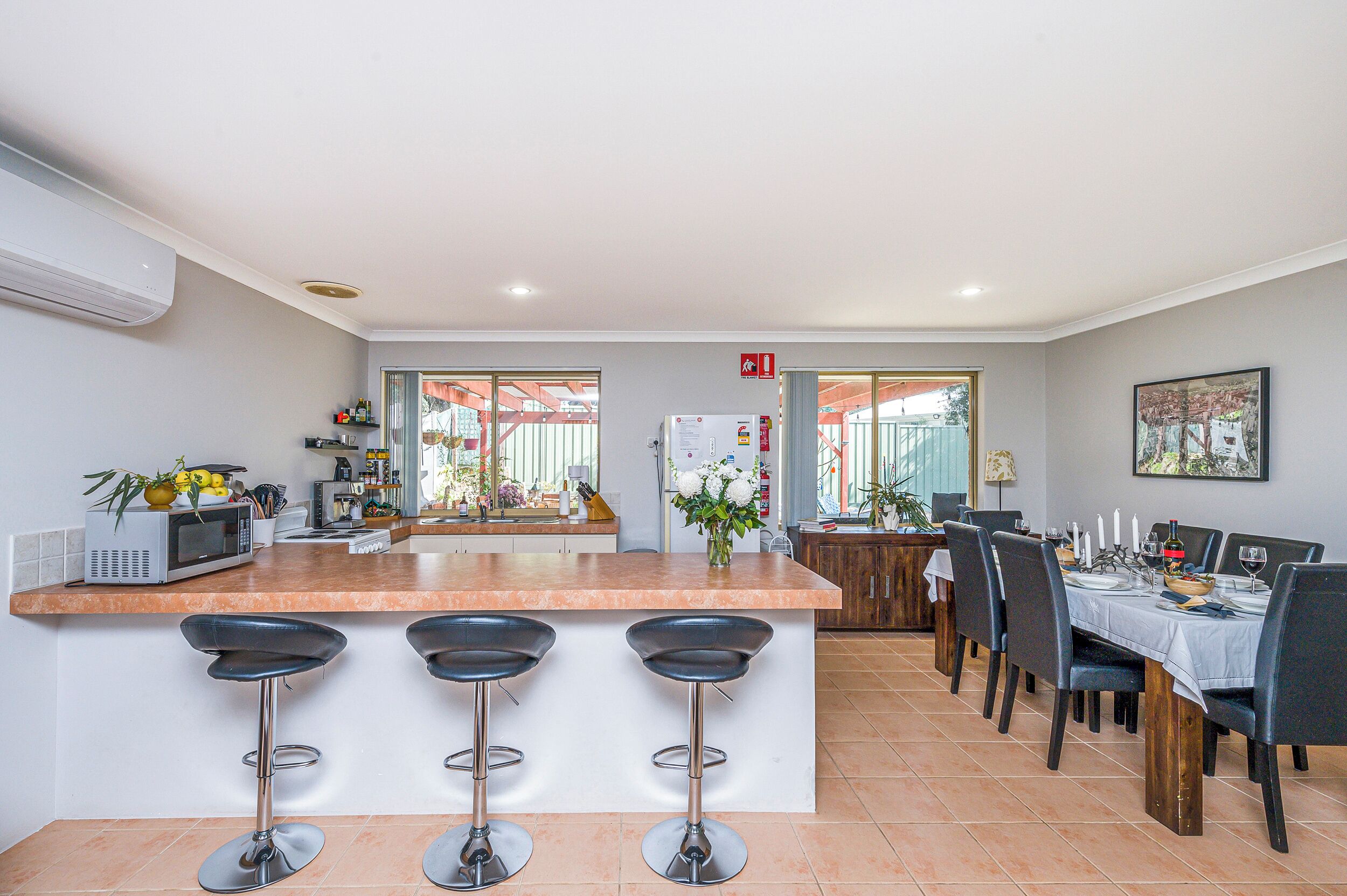 A modern kitchen with a central island, bar stools, a dining area with a table set for four, and a view of the outside.