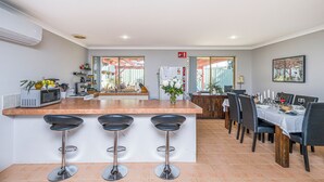 Uma cozinha moderna com uma ilha central, banquetas, uma área de jantar com mesa posta para quatro e vista para o exterior.