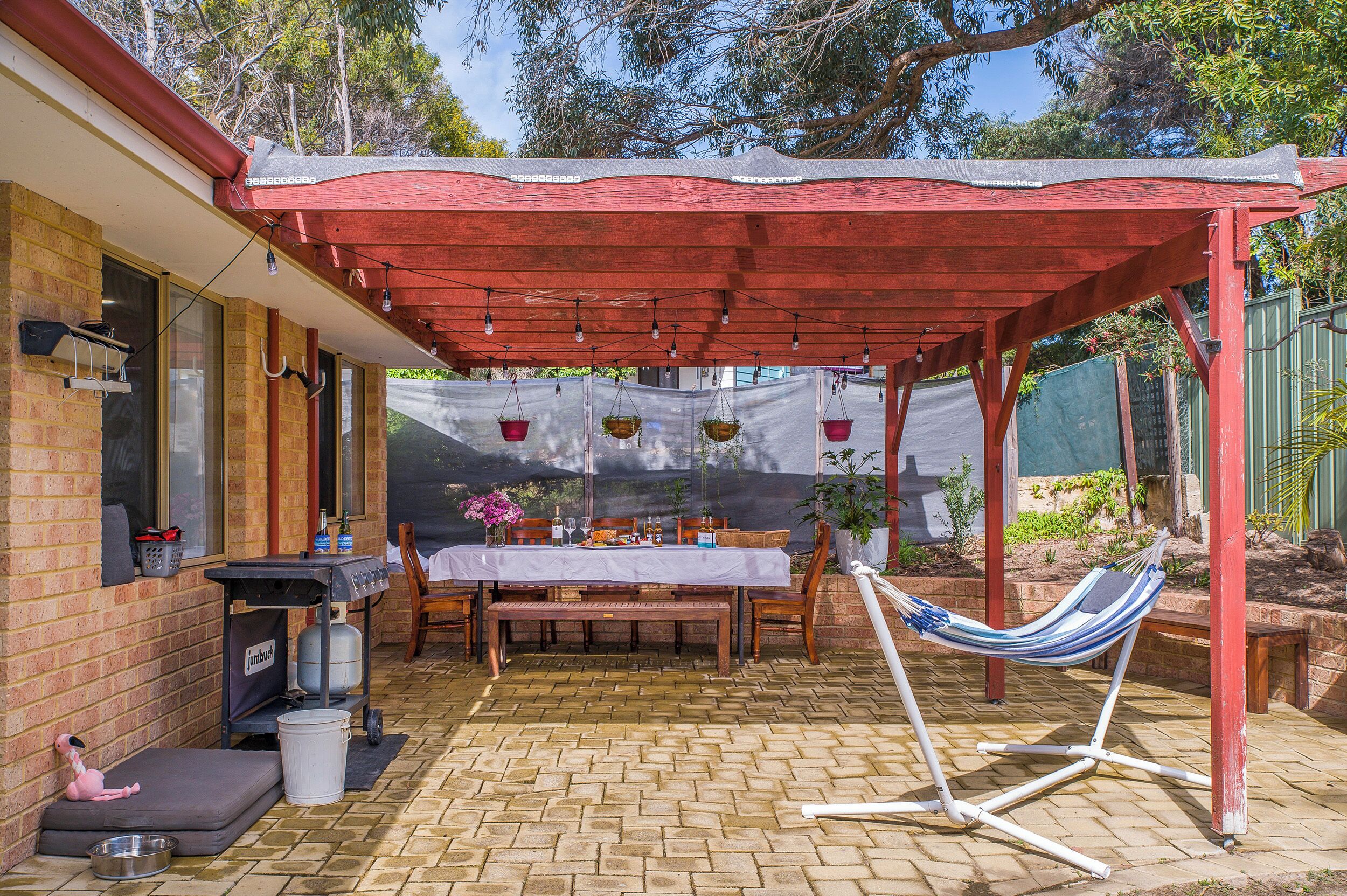 A covered patio area with a table set for dining, a hammock, and a barbecue grill.