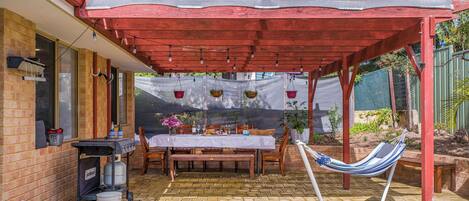 A covered patio area with a table set for dining, a hammock, and a barbecue grill.