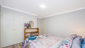 Une chambre à coucher avec un lit, une armoire, un miroir et une étagère sur laquelle est posé un vase de fleurs.