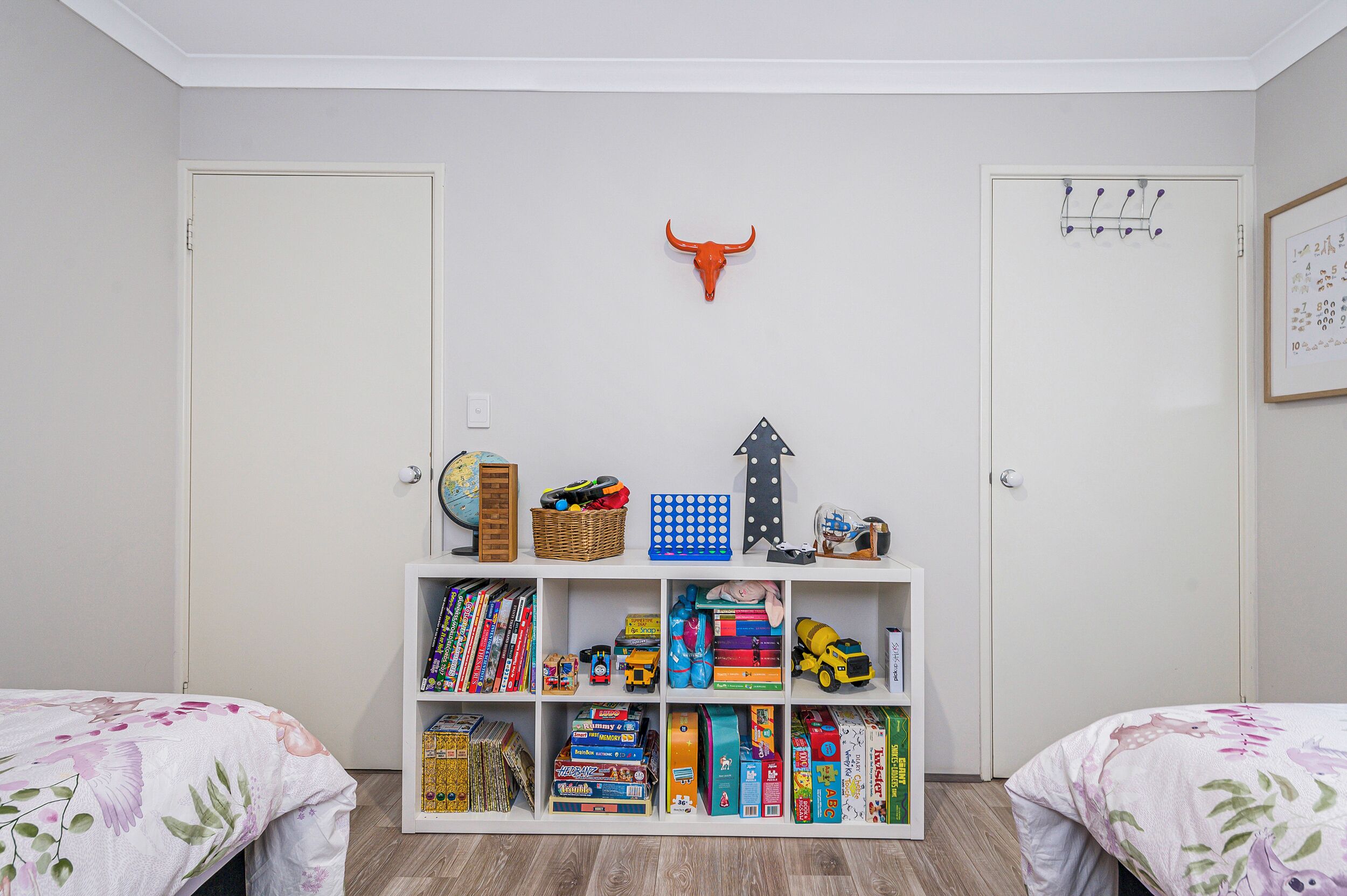 A child's room with two beds, a bookshelf filled with toys and books, a globe, and a wall-mounted bull head decoration.