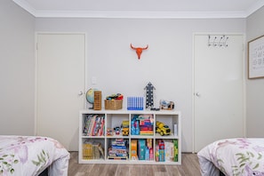 A child's room with two beds, a bookshelf filled with toys and books, a globe, and a wall-mounted bull head decoration.