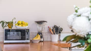 A kitchen counter with a microwave, a blender, a bowl of lemons, a bowl of bananas, and a plant.