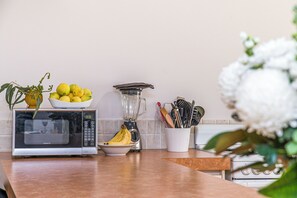 A kitchen counter with a microwave, a blender, a bowl of lemons, a bowl of bananas, and a plant. - Waves And Moore - Beautifully presented home (Guilderton)