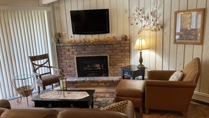 A living room with a fireplace, leather sofas, a glass coffee table, and a flat-screen TV mounted above the fireplace. - Cozy Mountain Retreat in Snowmass Village CO (Snowmass Village)