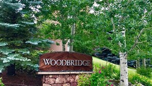 A wooden sign with the name "WOODBRIDGE" in a landscaped area with trees and shrubs. - Cozy Mountain Retreat in Snowmass Village CO (Snowmass Village)