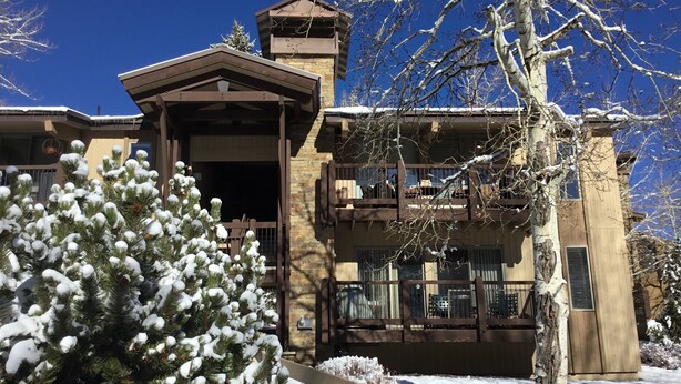 A two-story building with a stone facade, a wooden balcony, and a snow-covered pine tree in the foreground. - Cozy Mountain Retreat in Snowmass Village CO (Snowmass Village)