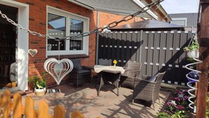 A patio with wicker furniture, a table with a vase, and a heart-shaped decoration. - Comfortable vacation home in a central location in Bad Zwischenahn with garden (Bad Zwischenahn)
