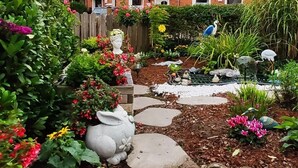 A garden with a stone pathway, various plants, and decorative statues. - Comfortable vacation home in a central location in Bad Zwischenahn with garden (Bad Zwischenahn)