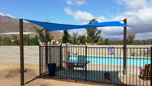 A fenced pool area with a table and chairs, a trash bin, and a dog.