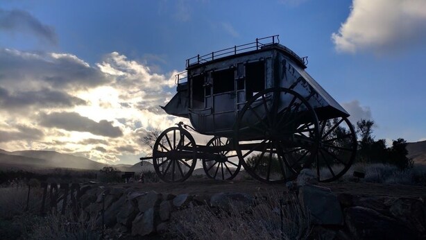 A stationary stagecoach with a platform and railings, set against a backdrop of a clear sky and distant mountains.