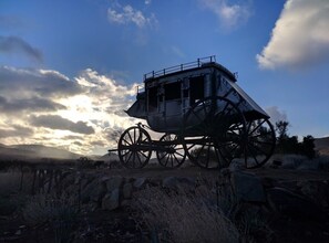 Un carruaje de época estacionado, con plataforma y barandillas, frente a un cielo despejado y montañas lejanas.