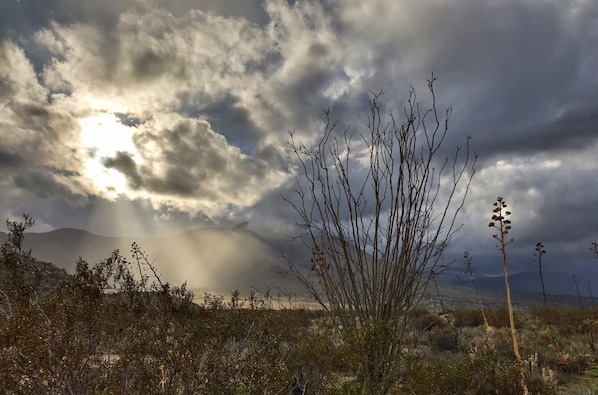 A landscape with a mountain in the background, a cloudy sky, and sparse vegetation in the foreground.