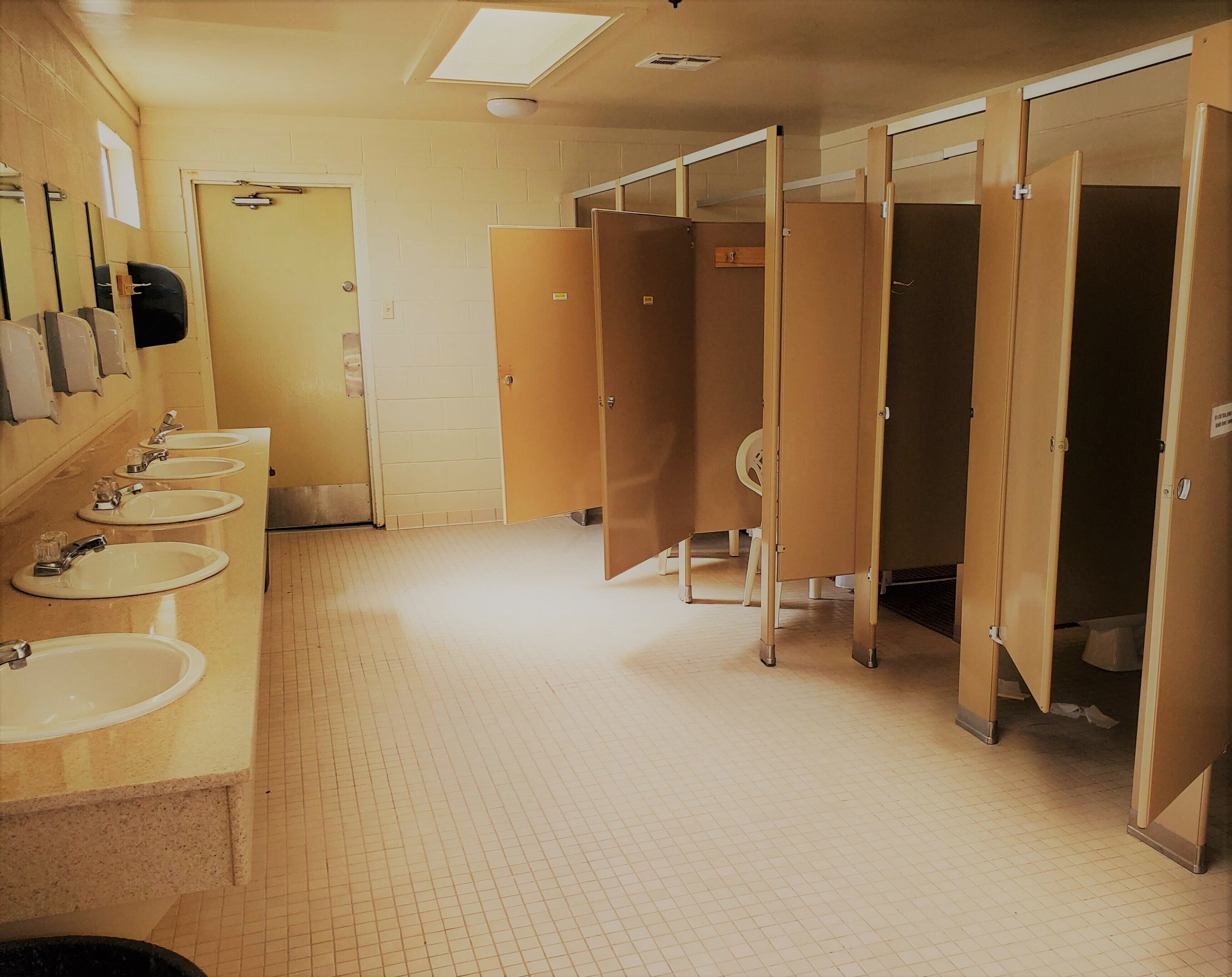 A public restroom with multiple sinks, a mirror, and wooden stalls.