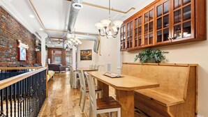 Un interior de restaurante con pared de ladrillo, mesas de madera, sillas blancas y un mueble de madera con puertas de vidrio.