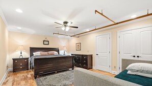 Un dormitorio con cama, mesitas de noche, ventilador de techo, cómoda y una puerta.