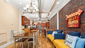 A modern kitchen with wooden cabinets, a dining area with a wooden table and chairs, and a living area with a sofa and cushions. - The Dolly Parton-Printer's Alley- 2 Blocks to Broadway (Nashville)