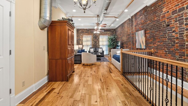 A spacious hallway with wooden flooring, a brick wall, and a staircase with a wooden railing. - The Dolly Parton-Printer's Alley- 2 Blocks to Broadway (Nashville)