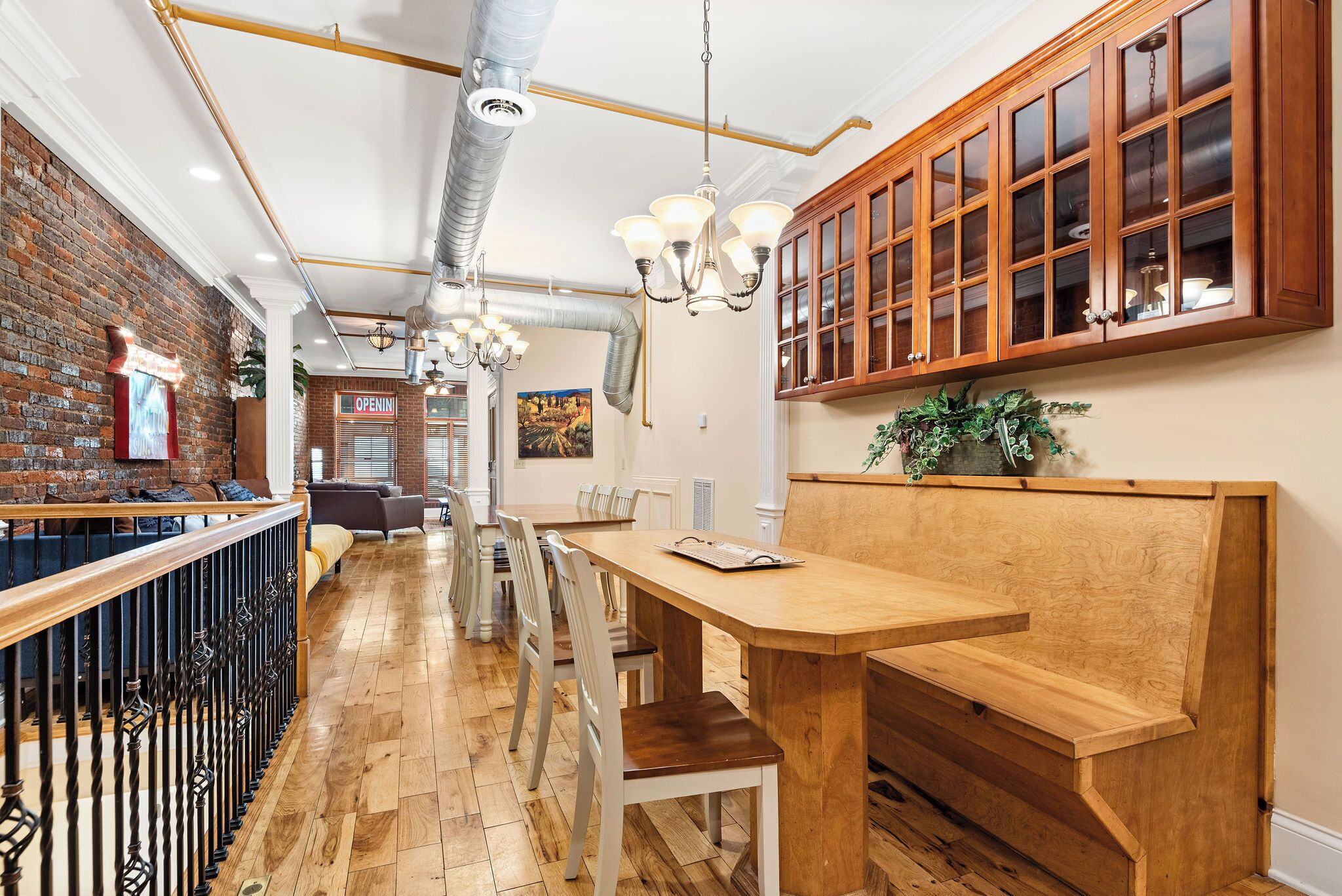 A restaurant interior with a brick wall, wooden tables, white chairs, and a wooden cabinet with glass doors.