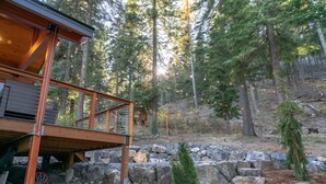 A wooden deck with a stone pathway leading to a cabin in a forested area. - Mountain Retreat, steps from Skiing, Mountain Biking, and Hiking (Wenatchee)