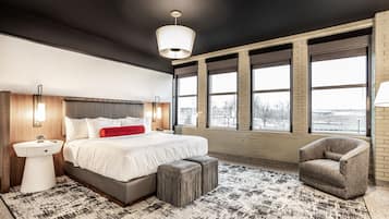 A modern bedroom with a large bed, a bedside table, a chair, and a view through large windows.