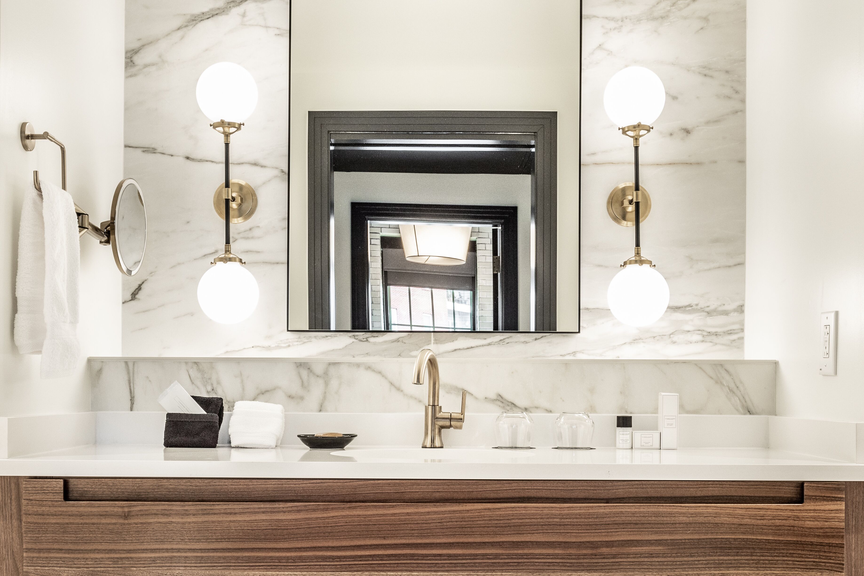 A bathroom with a marble sink, a gold faucet, and two wall-mounted lights.