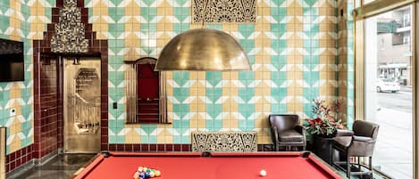 A pool table in a room with patterned walls, a door, and two chairs.