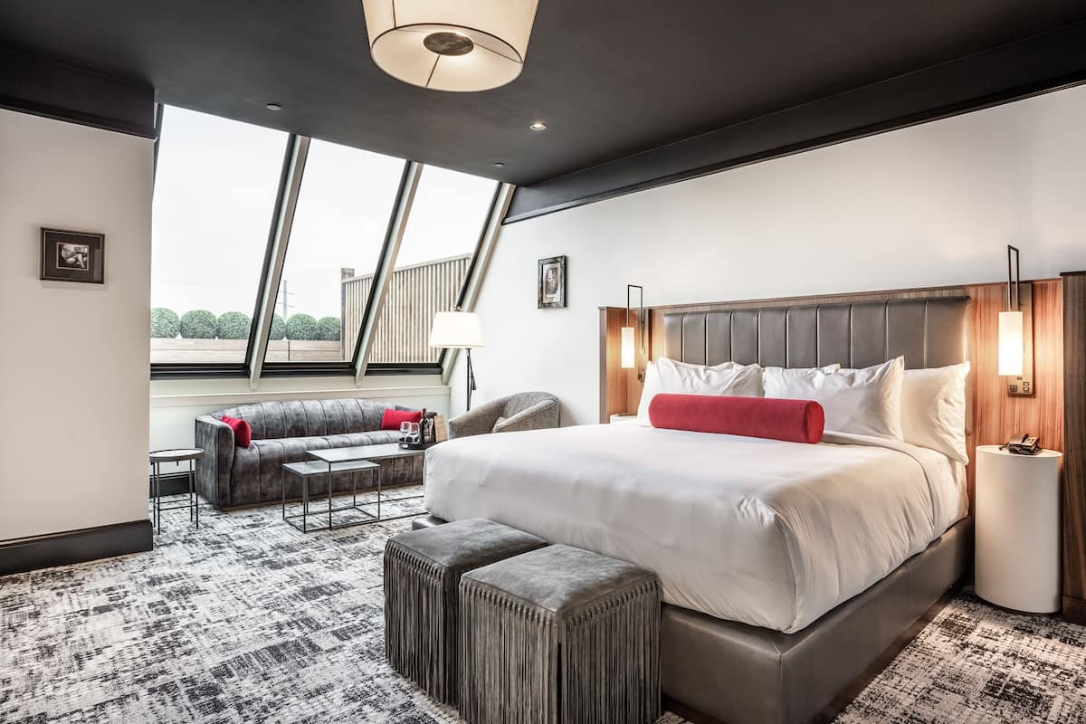 Ein modernes Hotelzimmer mit einem großen Bett, einer Sitzecke, einem kleinen Tisch und Blick ins Freie.
