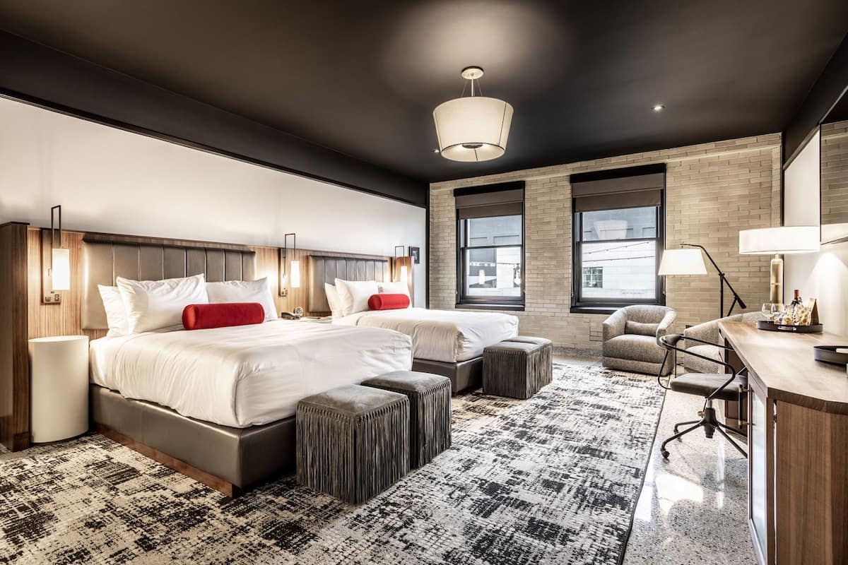 Ein modernes Hotelzimmer mit einem großen Bett, zwei Nachttischen, einem Schreibtisch, einem Stuhl und einem großen Fenster.