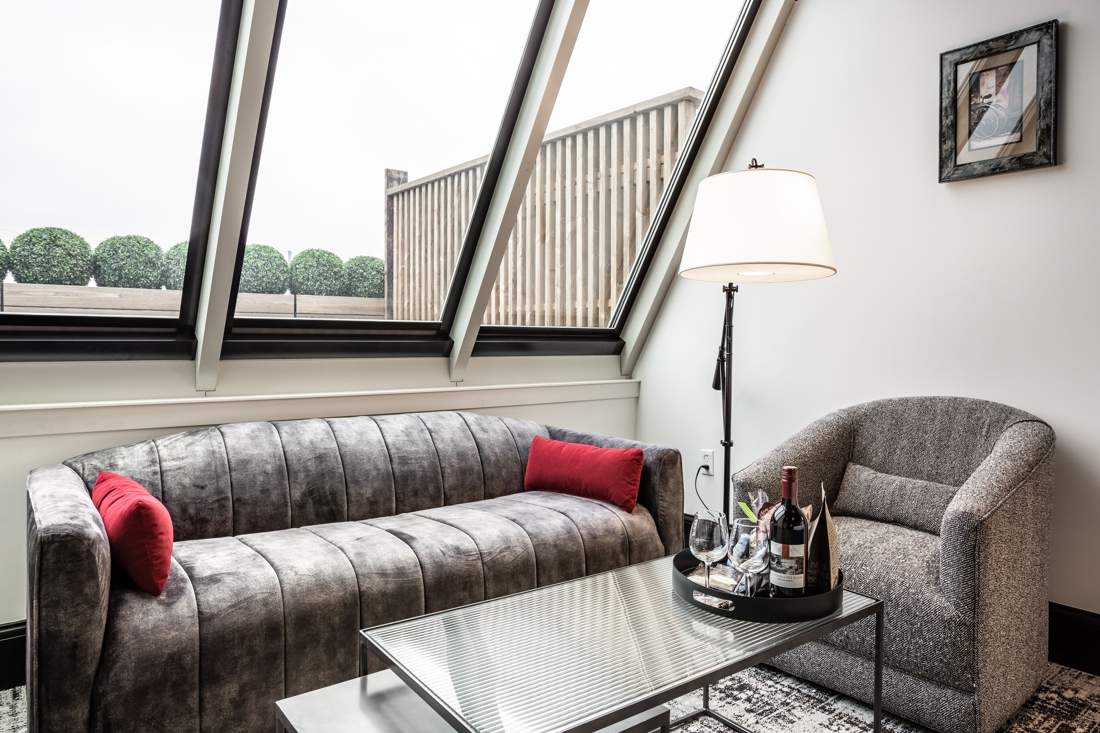 A modern living room with a grey sofa, a matching armchair, a glass coffee table, and a floor lamp.