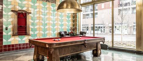 A pool table in a room with patterned walls and large windows.