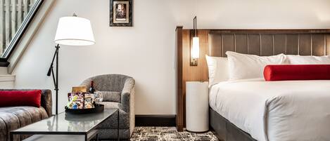 Una habitación de hotel con una cama, una silla, una mesa, una lámpara y un cuadro en la pared.