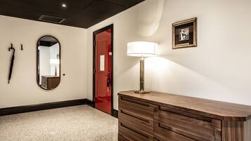A hotel hallway with a wooden vanity, a mirror, a red door, and a framed picture on the wall.