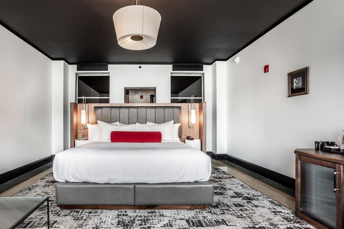 Ein modernes Hotelzimmer mit einem großen Bett, einem grauen Sofa, einem gemusterten Teppich und einer Deckenleuchte.