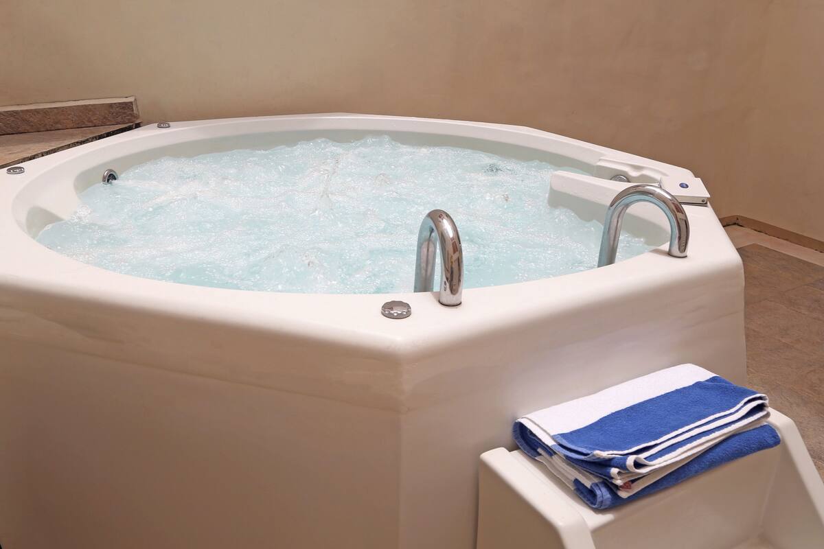 Eine weiße Badewanne mit fließendem Wasser, einer Armaturenkonsole und einem Handtuchhalter mit gefalteten Handtüchern.