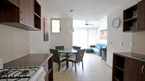 Una cocina moderna con estufa a gas, mesa de comedor y sillas. Hay una sala de estar con sofá y un reloj en la pared.