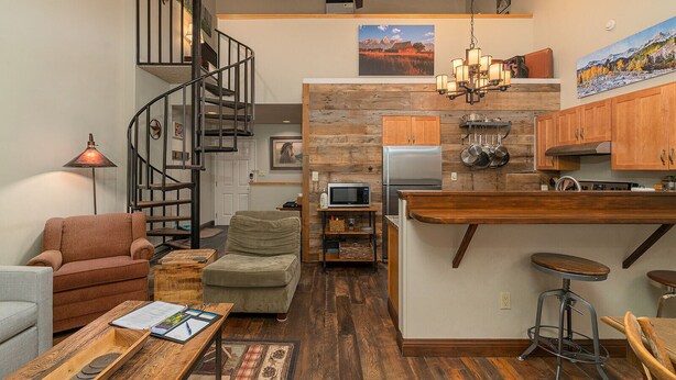 A modern kitchen with a central island, wooden cabinets, and a spiral staircase leading to an upper level.