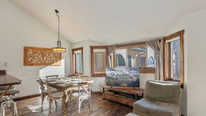 A cozy living room with a wooden dining table, chairs, a sofa, and a TV.