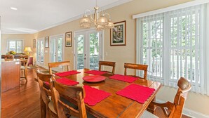 Uma sala de jantar com uma mesa de madeira, jogos americanos vermelhos e um candelabro.