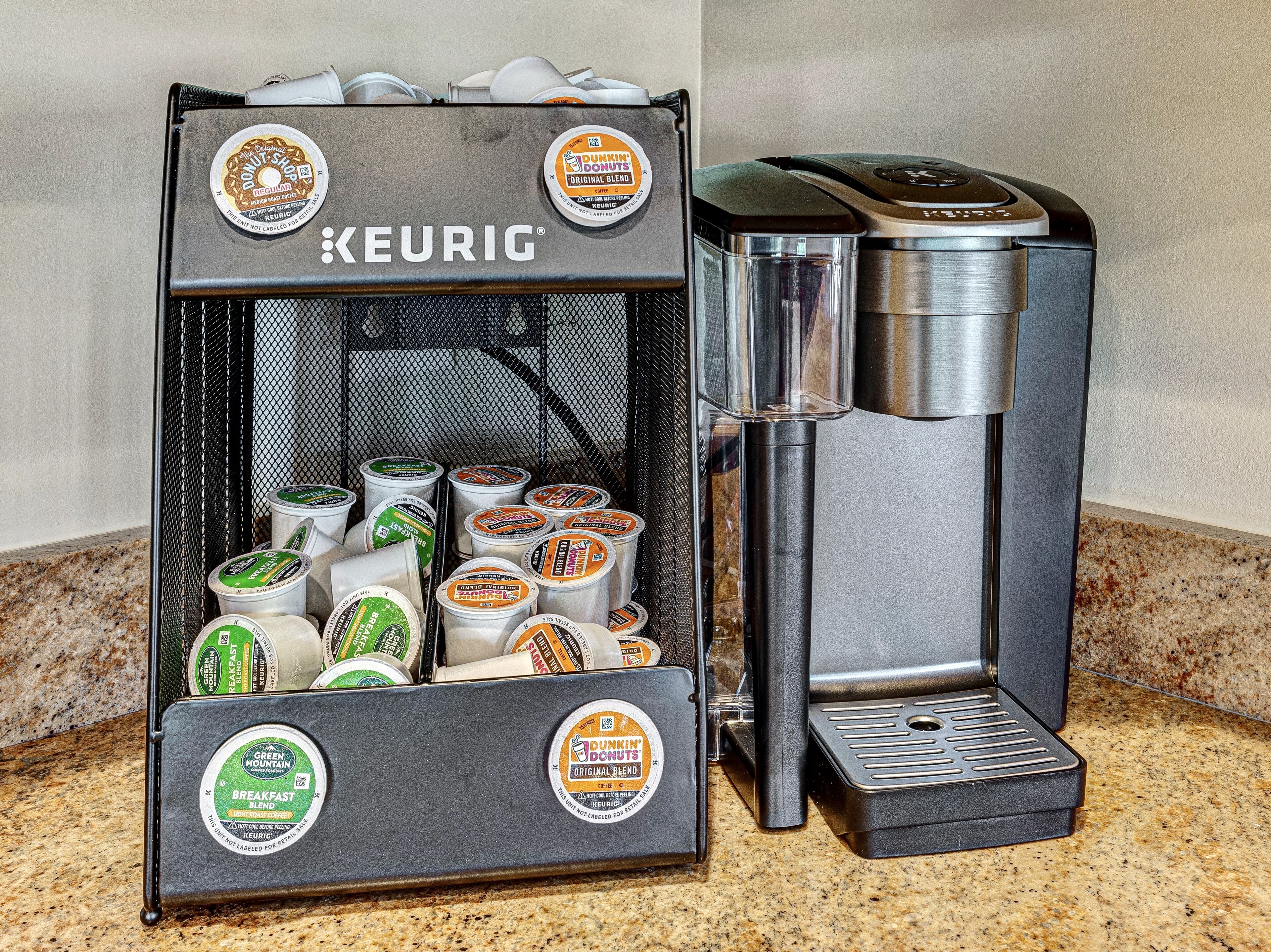 Una macchina per caffè Keurig con diverse capsule di caffè, tra cui marche come Dunkin' Donuts e Green Mountain, su un ripiano in granito.
