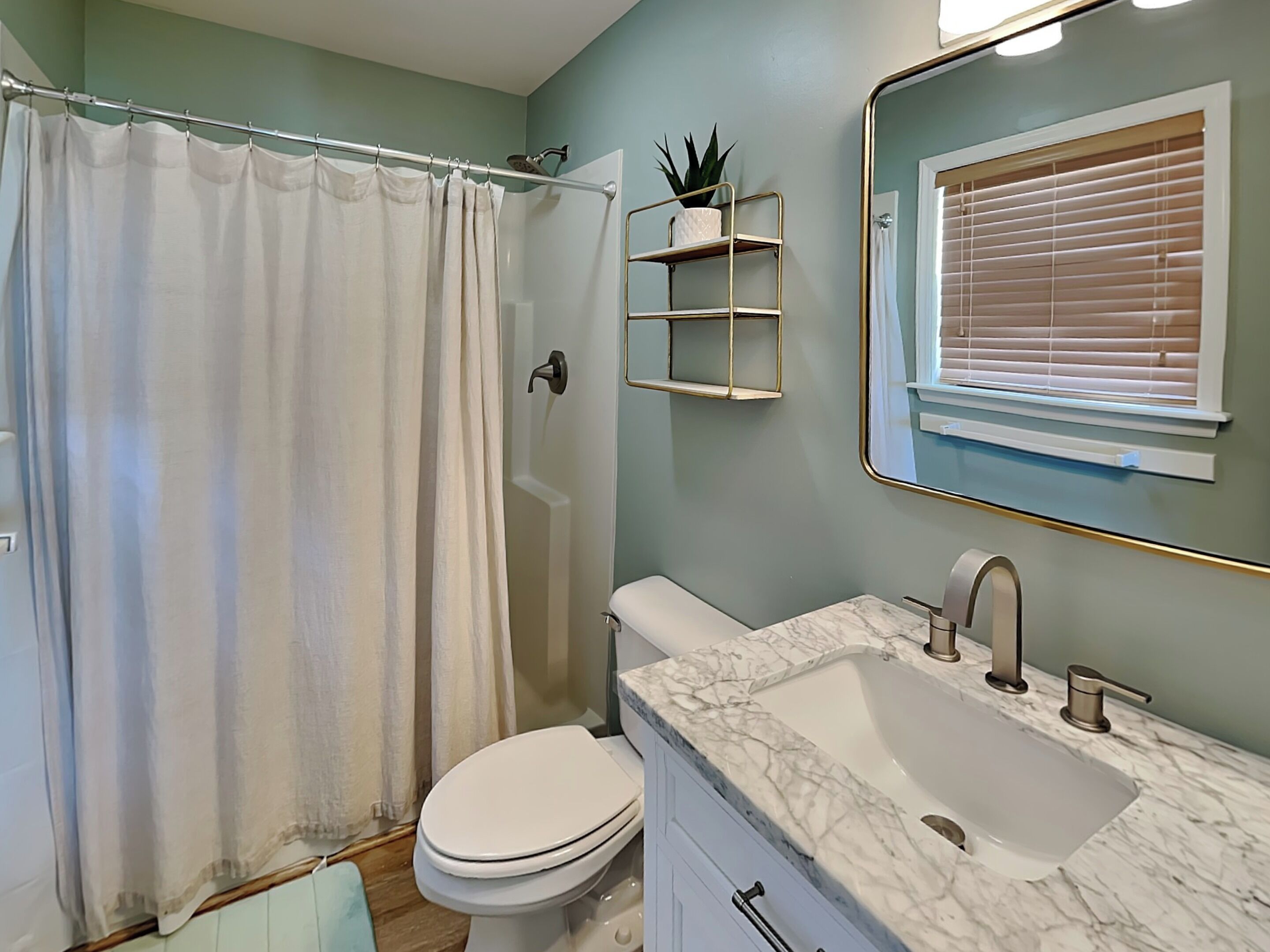 A bathroom with a shower curtain, toilet, sink with marble countertop, and a mirror with a gold frame.