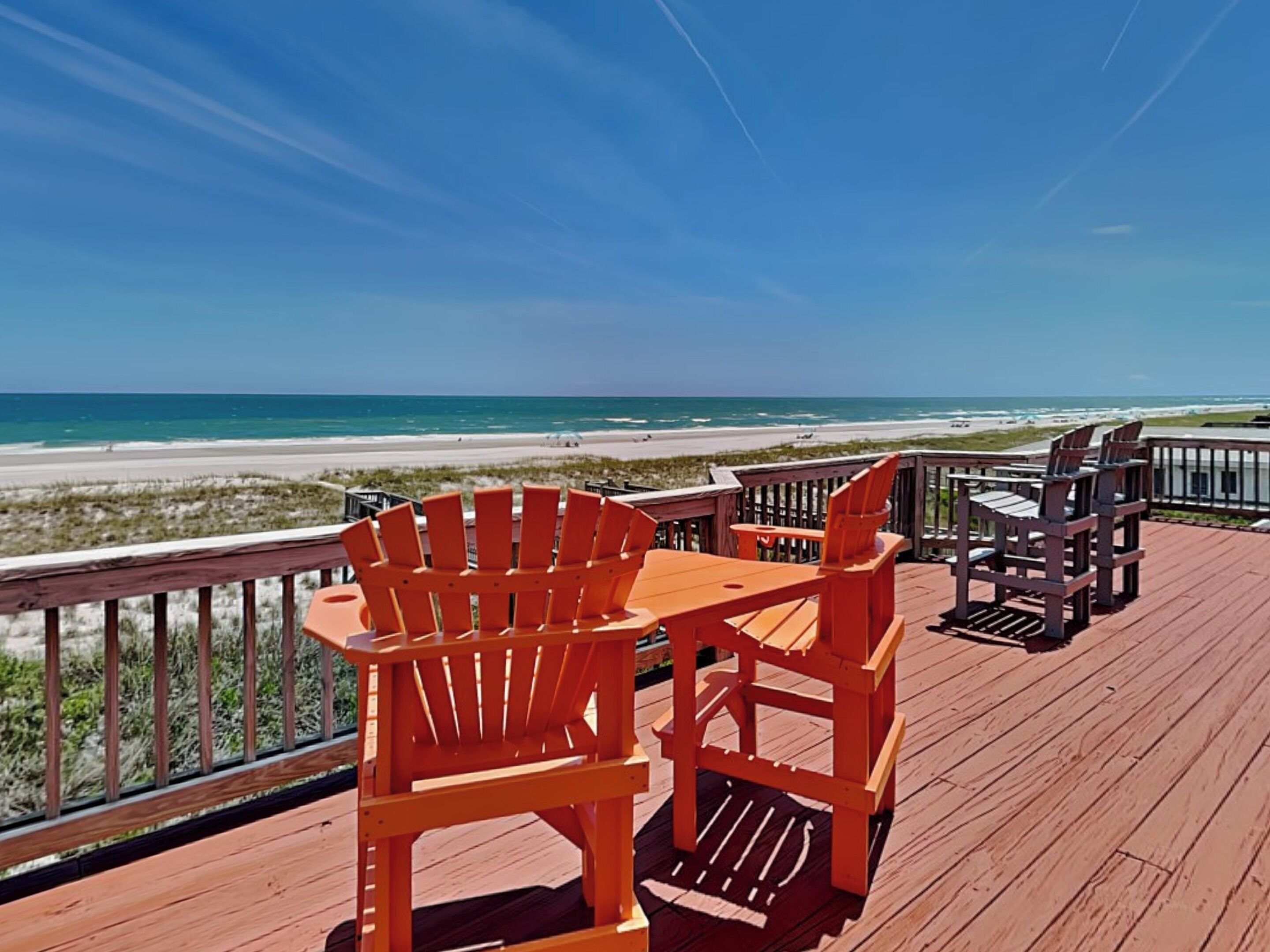 A wooden deck with outdoor seating, overlooking a beach and ocean.