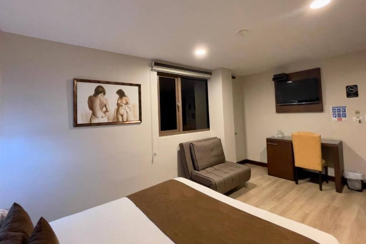 A hotel room with a bed, a sofa, a desk, a TV, and a window.