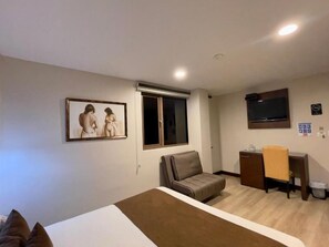 Una habitación de hotel con una cama, un sofá, un escritorio, un televisor y una ventana.