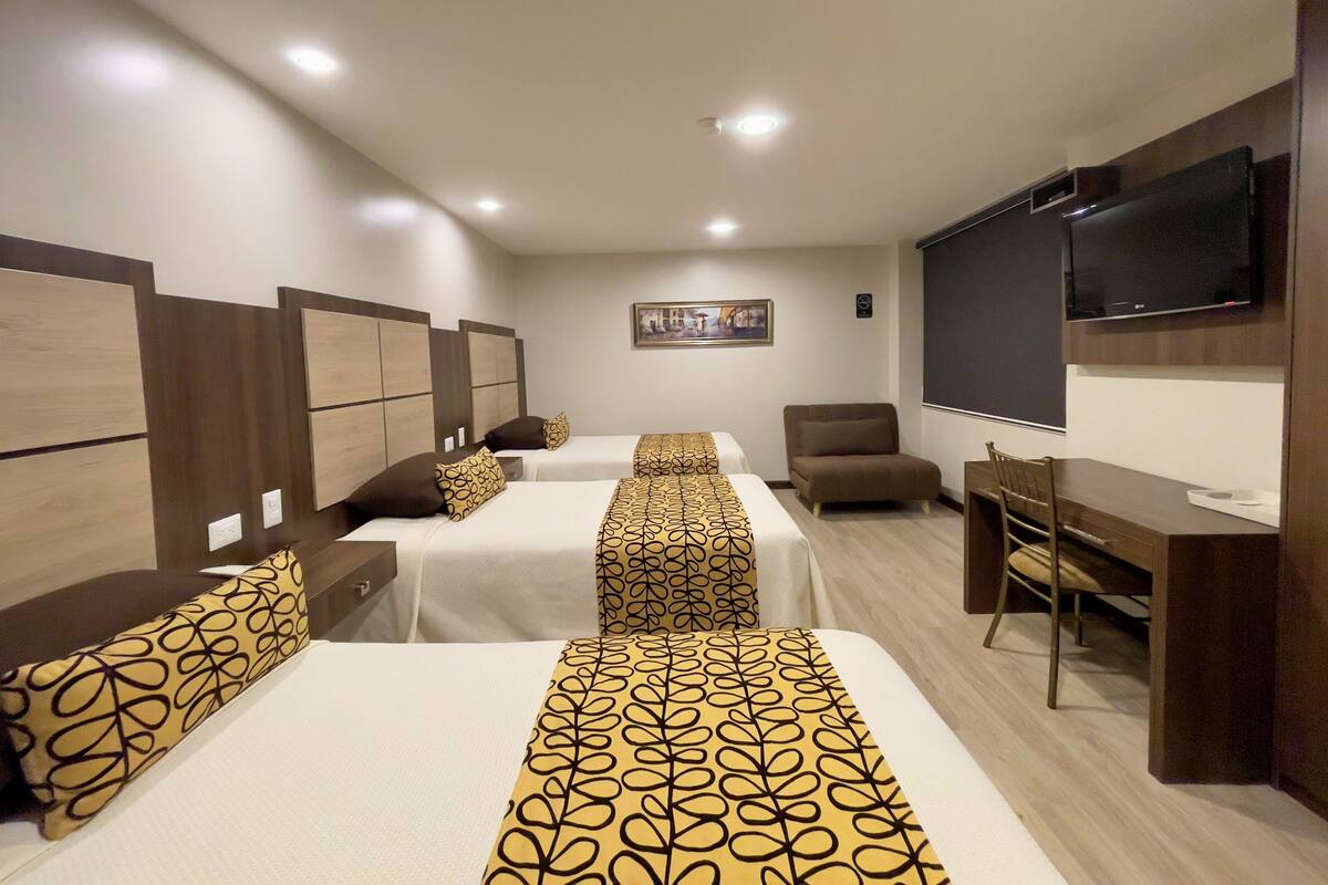 A hotel room with three beds, a desk, a chair, a television, and a painting on the wall.