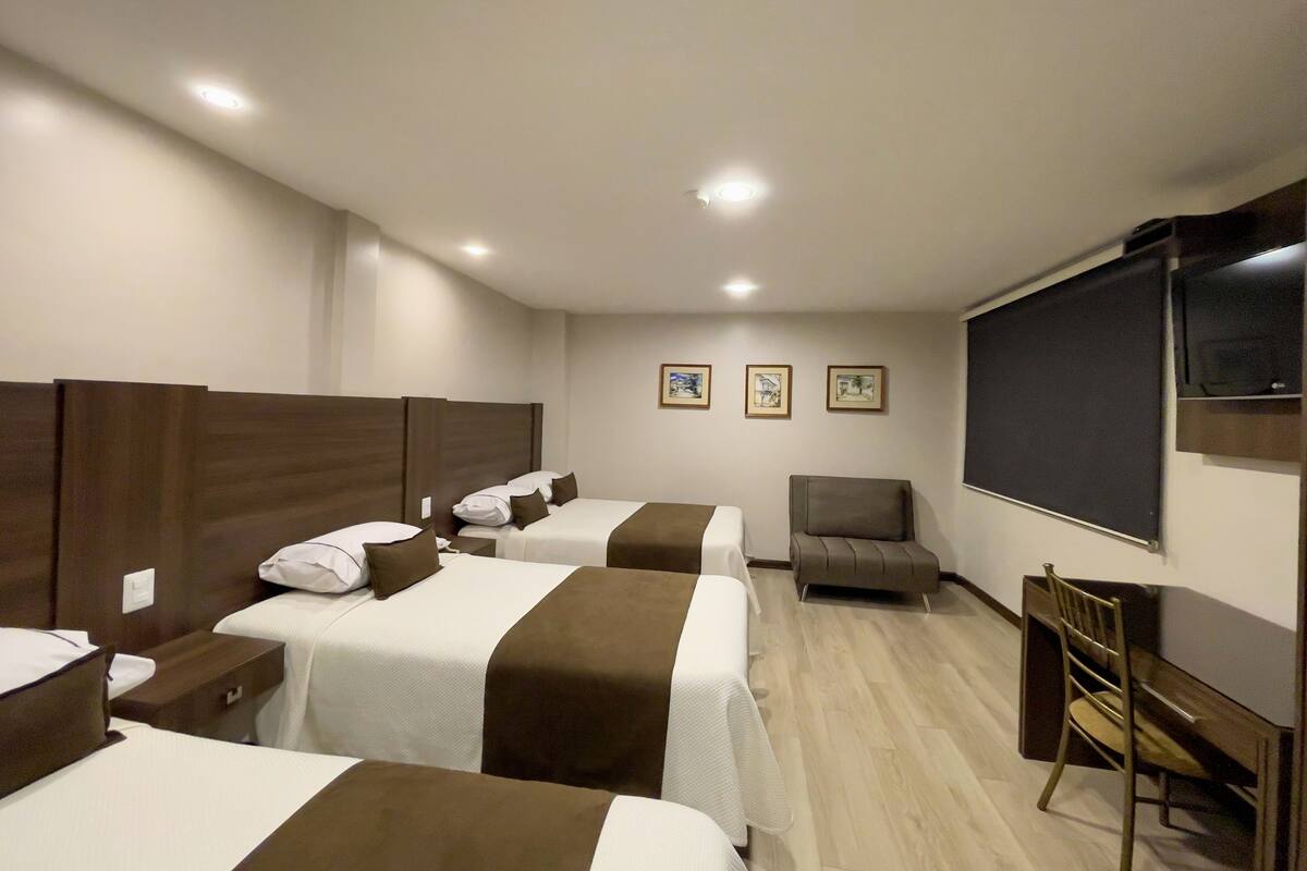 A hotel room with three beds, a desk, a chair, and a television.