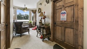 A cozy entryway with a wooden door, a dark leather chair, a table with a lamp, and a view of the outdoors. - Twisters Bed and Breakfast (Guernsey)