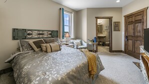 A bedroom with a large bed, a desk, and a chair. There is a window with curtains, a door, and a mirror. - Twisters Bed and Breakfast (Guernsey)